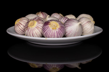 Wall Mural - Lot of whole fresh purple single clove garlic on white ceramic plate isolated on black glass