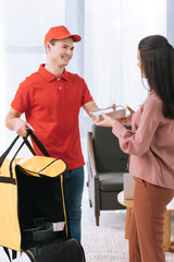 Wall Mural - Smiling delivery man with thermo bag giving food container to woman at home