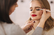 © Aleksandr - Makeup artist applies eye shadow, perfect evening makeup. Beauty blond hair girl with perfect skin and red lipstick