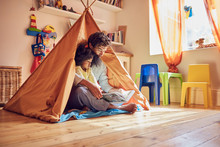 Father And Toddler Daughter Reading Book In Teepee