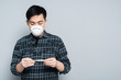 © LIGHTFIELD STUDIOS - young asian man in respirator mask looking at thermometer on grey background
