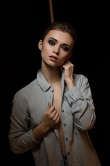 Wall Mural - Portrait of stylish fashionable brunette woman model in gray shirt posing near chair on black studio background.