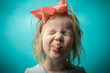 girl is mischievous. rebellious child. little girl with a pink bow on a blue background. girl shows his tongue