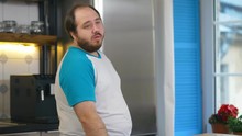 Sad and hungry overweight man opening and closing fridge being on healthy diet