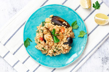 Seafood Risotto In A Blue Plate On A Gray Background, Top View. Risotto With Shrimp, Tomatoes, Parsley And Mussels In Shells. Tasty And Healthy Mediterranean Cuisine.