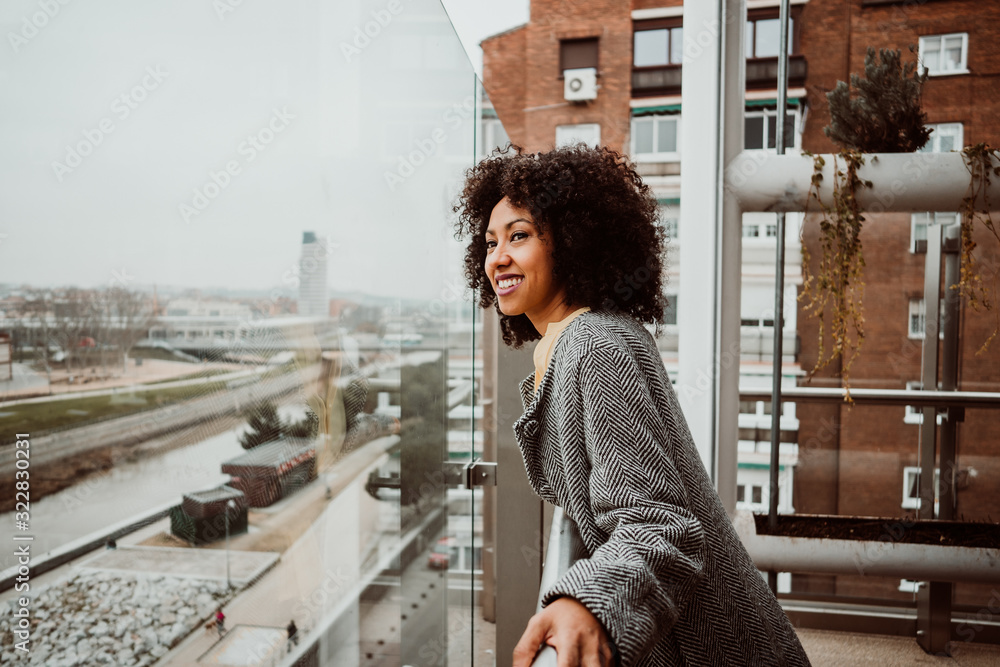.Beautiful African American woman looking out the window of a tall building overlooking the city of Madrid. Relaxed and carefree. Lifestyle - obrazy, fototapety, plakaty 