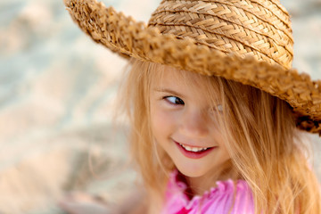 Wall Mural - portrait of a little blonde girl in a straw hat in summer on a sandy beach, space for text