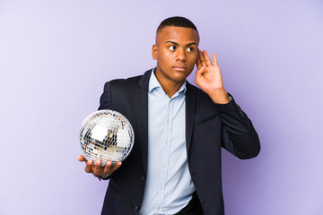 Wall Mural - Young latin man holding a ball party isolated trying to listening a gossip.