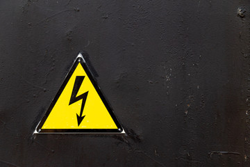 High voltage sing on a black painted metal surface of protective electrical industrial equipment background with copy space.