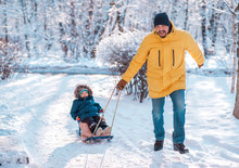 Winter Walk: Dad Sledging With Son. Father Pulling Sled With Toddler Son In Snowy Day. Man And Child Enjoy Ride And Smile. Focus On Face Of Father. Family Fun, Happy Childhood And Activity Outdoors