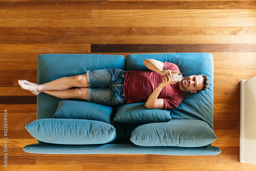Casual guy on armchair with smartphone - obrazy, fototapety, plakaty 