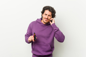 Wall Mural - Young man holding a vaporizer covering ears with hands.