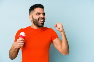 Wall Mural - Young latin man holding an ice cream isolated raising fist after a victory, winner concept.