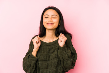 Young chinese woman isolated on a pink background raising fist, feeling happy and successful. Victory concept.