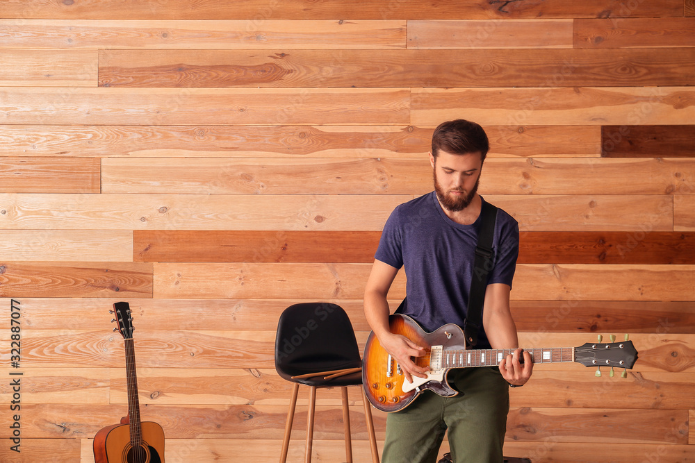 Young man playing guitar near wooden wall