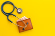 Doctor stethoscope and the new leather brown men wallet on yellow background. Budget for health check or money and financial concept