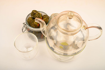 Flower tea balls in a glass jar, a glass teapot and a glass on a white background. Close up.