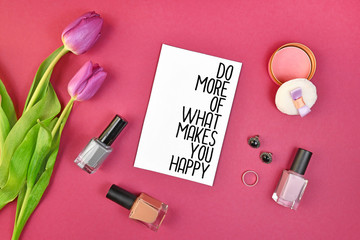 Happiness motivational concept with sign saying 'Do more of what makes you happy', surrounded by spring flowers and female accessories like makeup on pink background, flat lay