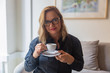 © Mangostar - Front view of smiling mature businesswoman holding cup of coffee. Confident lady in eyeglasses looking at camera. Drink, confidence concept