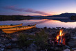 © sanderstock - Campfire during dusk at the shore of a lake with two kayaks. Sweden.