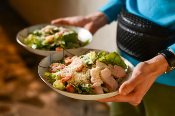 Waiter holds two plates with Italian salad with jamon, prosciutto, fresh vegetables and parmesan cheesein a restaurant