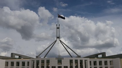 Wall Mural - Australian national flag on tall flagpole agains blue sky waving over the federal parliament house.