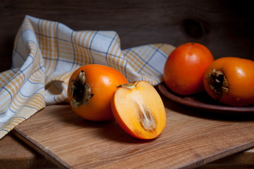 Whole ripe persimmon and sliced fruit on a wooden background..