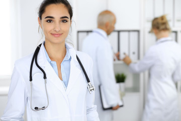 Doctor woman in clinic with colleagues at the background. Hispanic or latin american staff in medicine