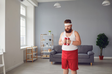 Wall Mural - Funny fat man with dumbbells doing exercises in the room.