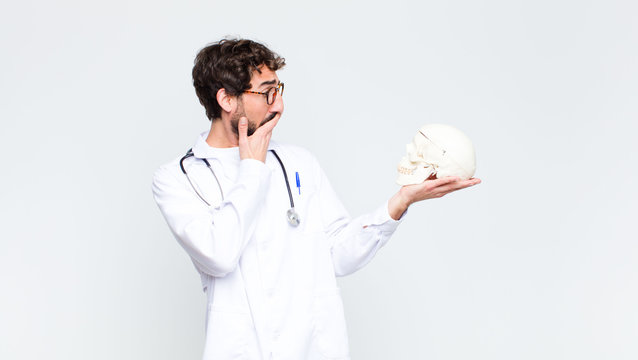 young crazy bearded doctor man holding a human skull