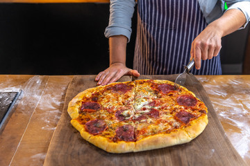 Wall Mural - Female chef is cutting a freshly made, delicious traditional pizza