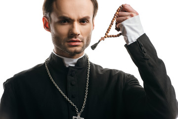 Wall Mural - young, serious catholic priest holding wooden rosary beads while looking at camera isolated on white