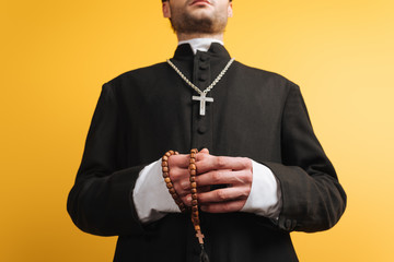 Wall Mural - low angle view of catholic priest holding wooden rosary beads isolated on yellow