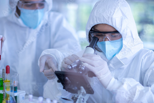 Fotografía A female scientist wearing a mask and looking through the microscope in the labo