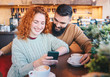 © Sanja - A couple sitting in a cafe, looking at a cell phone and drinking coffee.