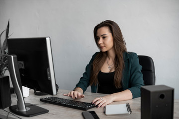 Brunette woman is working in front of a monitor in a office. Business woman working at computer at coworking space. Portrait of happy lady typing at workplace. Female professional working with pc.