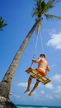Beach Summer Vacation Tropic Palm Style Portrait Of Young Handsome Man On Beach Swing Blue Sea.Man Swinging On The Beach On Phu Quoc Island, Vietnam. Happy Man Dangles On Tropical Palm Tree Swing.