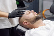 © klavdiyav - beard modeling in Barber shop, beard care for men, male beauty and care concept, applying the scrub to the face