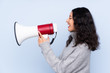 © luismolinero - Spanish Chinese woman over isolated blue background shouting through a megaphone