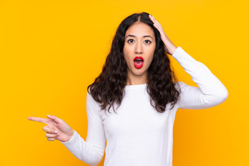 Canvas Print - Mixed race woman over isolated yellow background surprised and pointing finger to the side