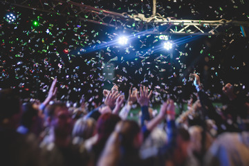 Colourful confetti explosion fired on dance floor air during a concert festival, crowded concert hall with scene stage lights, rock show performance, with people silhouette