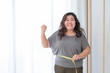 Asian obese women are happy because of size reduction after checking with tape measure.