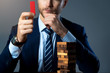 © whyframeshot - caucasian businessman formal suit hand hold important wooden block and  focus with wooden stack tower strategy organization business ideas concept dark background