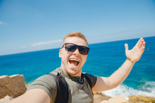 Happy Traveler Man Taking Selfie Photo In Sunglasses On Background Of Bruise Sea With Backpack. Travel Concept