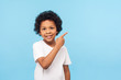 © khosrork - Look, advertise here! Portrait of cute cheerful little boy with curly hair in white T-shirt pointing to empty place on background, preschooler showing copy space for promotional ad. indoor studio shot