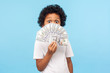 © khosrork - Amazed cute funny little boy with curly hair in T-shirt hiding half face with money and peeking out of dollar bills with astonished shocked eyes. indoor studio shot isolated on blue background