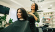 © My Ocean studio - Premium service. Close-up photo of a young hairstylist cutting hair of her happy female client who is looking in the mirror while sitting in an armchair.