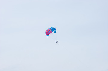 Red-blue parachute with two people in cloudy sky