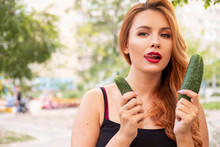 Beautiful Plus Size Woman Comparing Mens Penis Sizes Using Cucumber As An Example. Summer Hot Portrait Outdoor. Copy Space