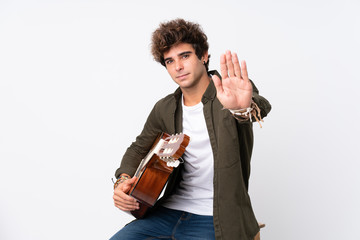 Wall Mural - Young caucasian man with guitar over isolated white background making stop gesture with her hand